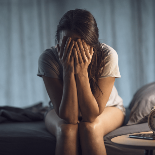 Jeune femme souffrant d'insomnie, assise sur son lit, se tenant la tête