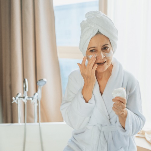 Femme âgée appliquant la crème nourrissante sur le visage