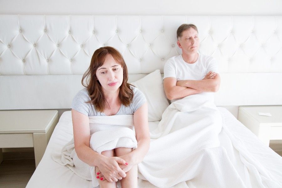 femme assise à coté de son mari dans un lit ayant des Problèmes de libido à la ménopause