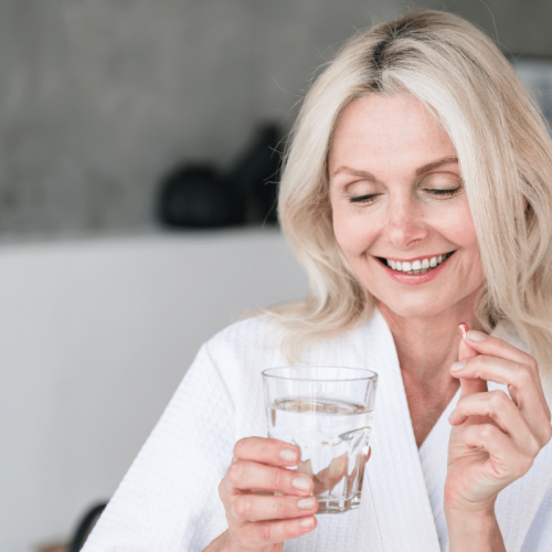 Une femme en ménopause qui tient une vitamine et un verre d'eau