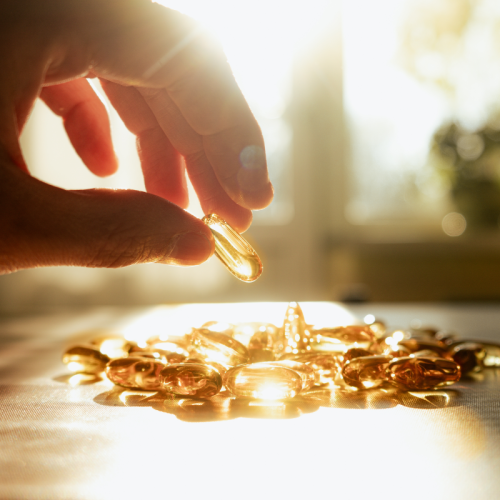 Main qui prend des gélules de vitamine D au soleil, sur une table ensoleillée.