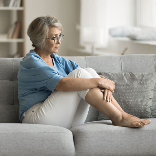 Une femme âgée assise sur son canapé, en état d'anxiété