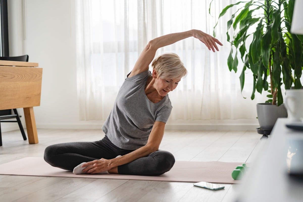 Femme âgée s'étirant sur un tapis exercices physiques ménopause