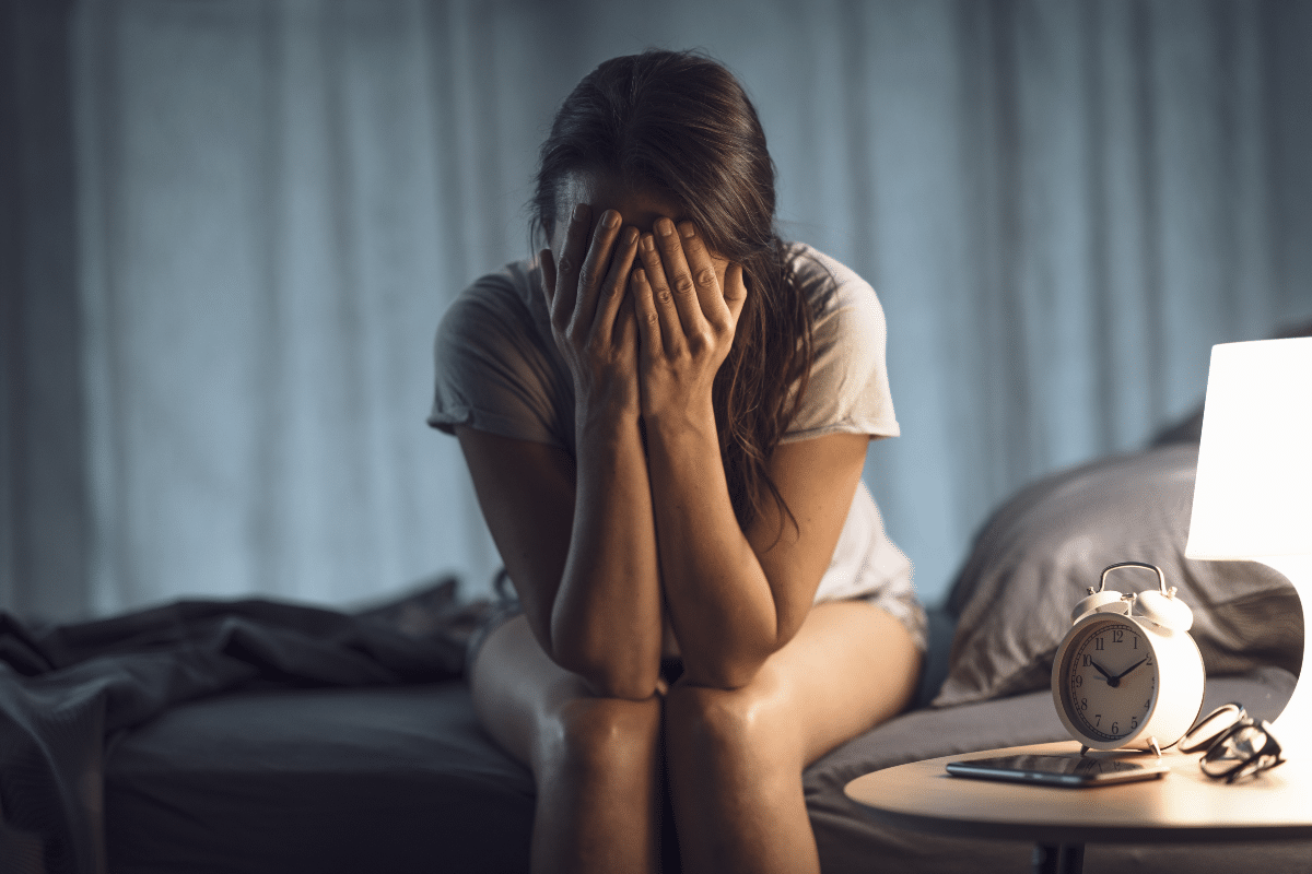 Jeune femme souffrant d'insomnie, assise sur son lit, se tenant la tête
