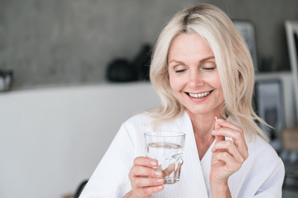 Une femme en ménopause qui tient une vitamine et un verre d'eau