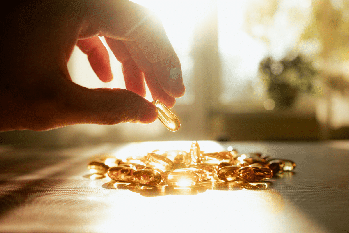 Main qui prend des gélules de vitamine D au soleil, sur une table ensoleillée.